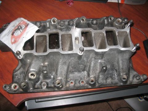 1991 Ford Bronco - A gray metal intake manifold with a gasket is shown on a wooden desk.