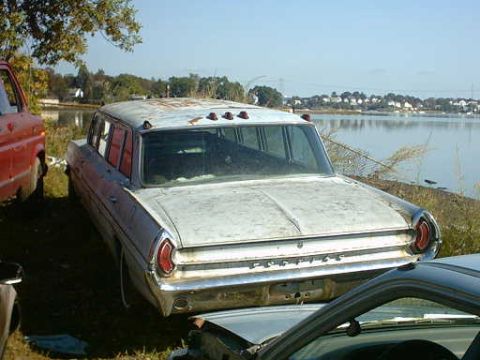 1962 Pontiac Starchief - A weathered white station wagon sits by the water, its rear end showing signs of age and neglect.