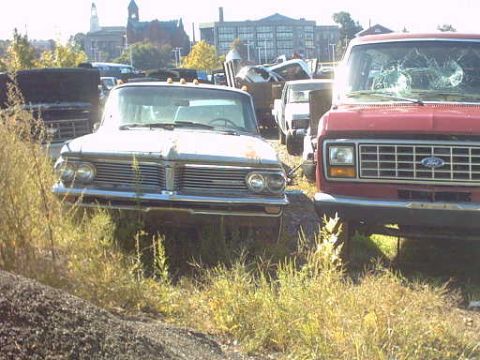 1962 Pontiac Starchief - A 1961 Pontiac Bonneville sits in a junkyard next to a red Ford van.