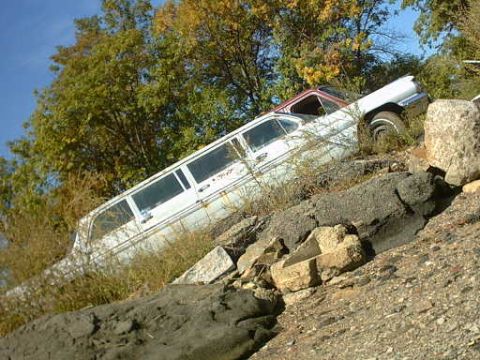 1962 Pontiac Starchief - A long white limousine with a red roof sits on a rocky slope, partially obscured by vegetation.