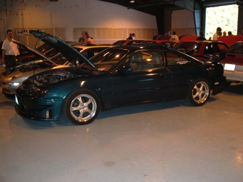 1991 Ford Probe - A dark green coupe is displayed indoors with its hood open, surrounded by other vehicles.