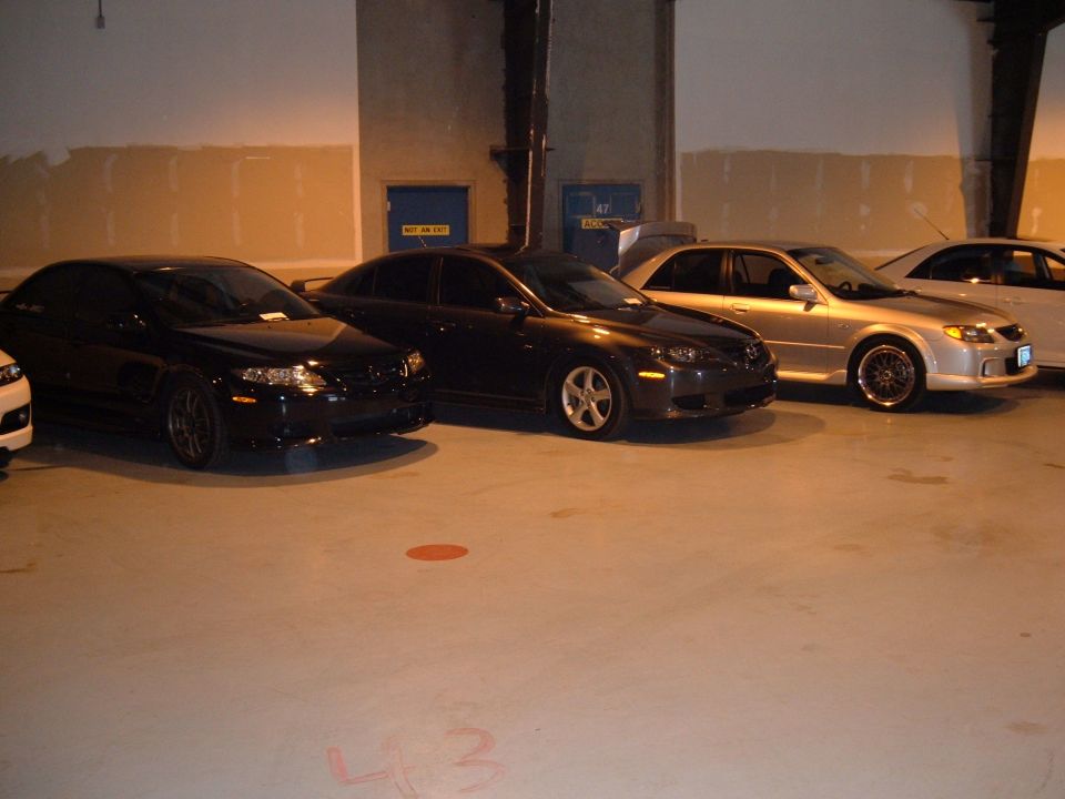 Three sedans parked in a garage, one silver, one dark gray, one black