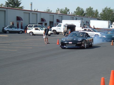 1991 Ford Probe - A black Mazda RX-7 FD performs a drift in a parking lot with other vehicles present.