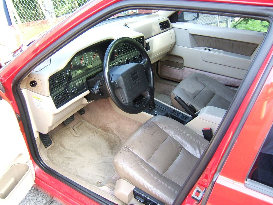 Interior view of a red Volvo 740 sedan showing dashboard, steering wheel, and seats