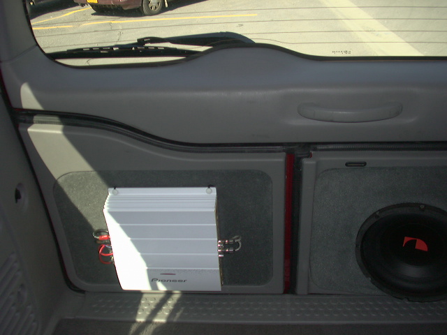 Cargo area of SUV showing white Pioneer amp on gray carpeted panel beside subwoofer enclosure