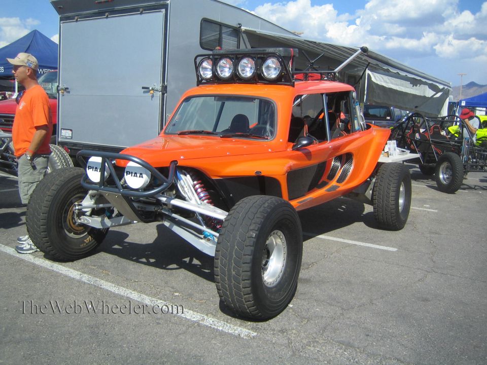 Orange off-road buggy with roof light bar parked in a paved event lot