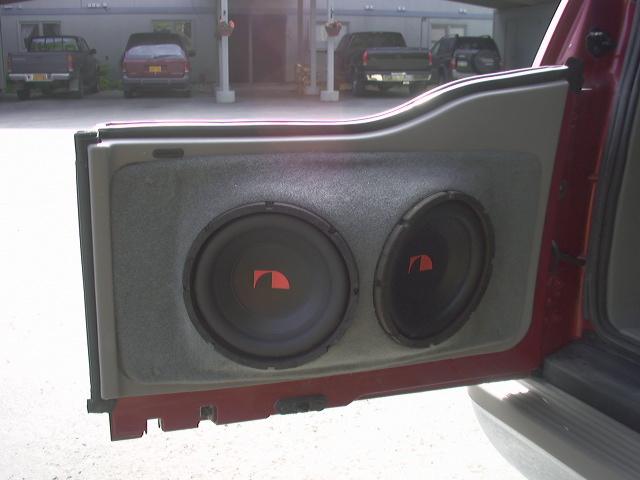 Dual subwoofer enclosure mounted in open dark red SUV door panel