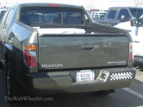 1990 Ford Bronco - rear of a dark green Honda Ridgeline 4WD pickup showing the tailgate badging, license plate and a Checkers plate frame in a parking lot.
