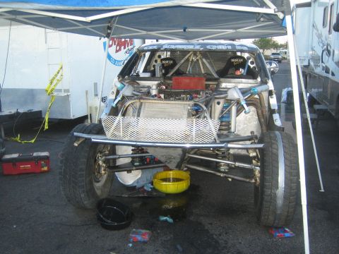 1990 Ford Bronco - race truck sits on jack stands under a pop-up canopy, its rear bodywork removed to expose the tubular chassis and rear suspension during pi…