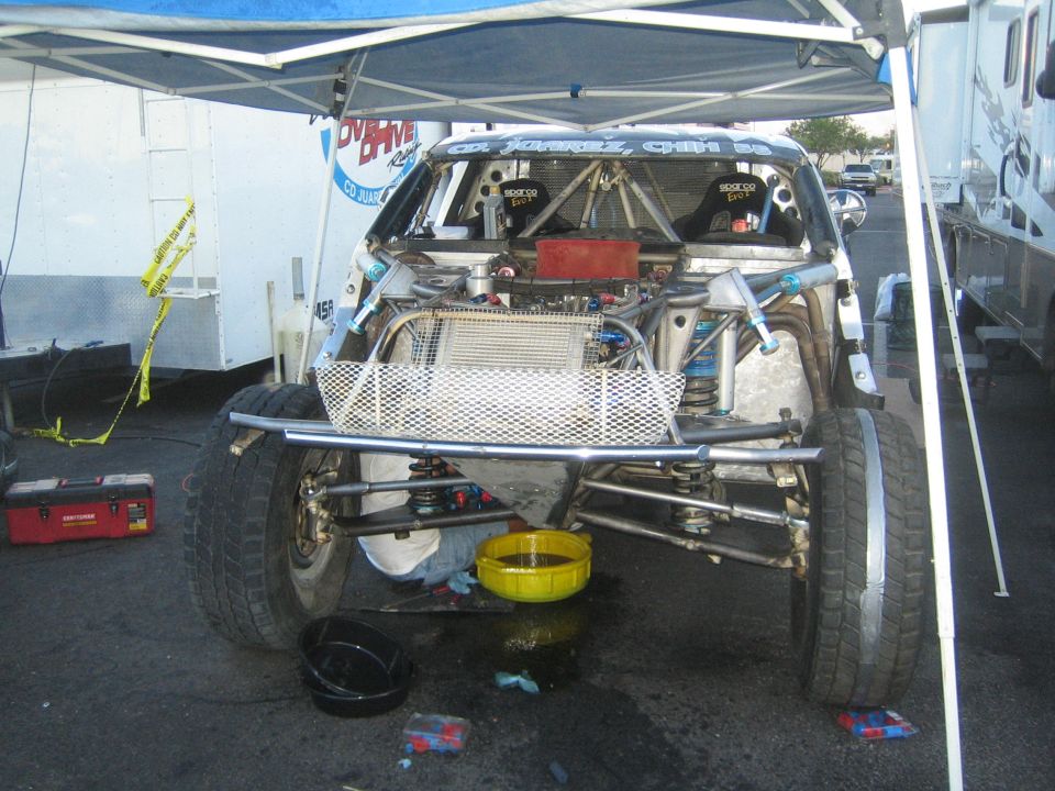 Rear of off-road race truck with tube chassis under a canopy in a paddock