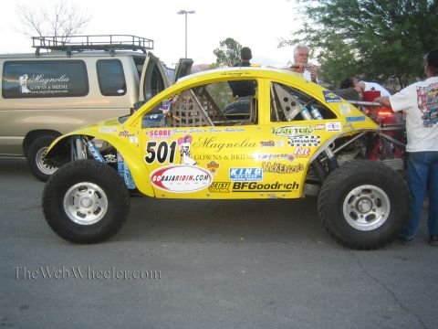 1990 Ford Bronco - yellow Volkswagen Beetle-bodied Baja racer, number 501, covered in sponsor decals including Magnolia Gowns and BFGoodrich.