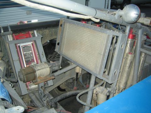 1990 Ford Bronco - close-up of an off-road vehicle's mounted radiator, a hydraulic bottle jack and shock absorbers within the dusty chassis.