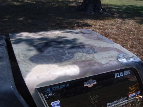 1988 Ford Bronco - The hood of a truck displays a worn camouflage paint job with visible primer and rust patches.