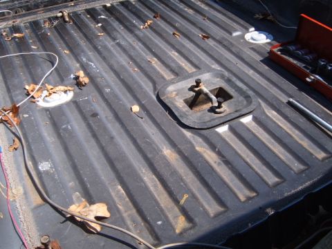 1988 Ford Bronco - Close-up of a truck bed showing a tie-down anchor and ribbed flooring, with a toolbox in the background.