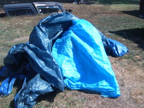 1988 Ford Bronco - Vehicle parts are covered by tarps, with a portion of a vehicle's roof visible in the background.