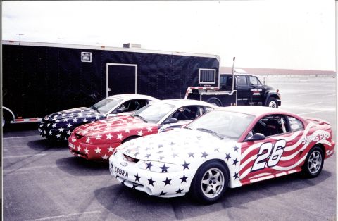 1995 Ford Mustang - Three 1995 Ford Mustangs, painted with stars and stripes, are lined up in front of a trailer and truck.