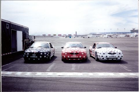 1995 Ford Mustang - Three 1995 Ford Mustangs, each adorned with a patriotic star graphic, are lined up at a racetrack. The word 'COBRA' is visible on the front…