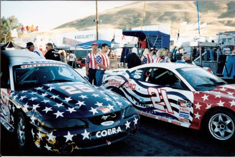 1995 Ford Mustang - Two Ford Mustangs, one numbered 25 and the other 21, display patriotic star-spangled liveries at a race event.