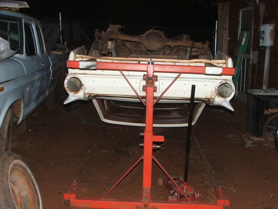 Car body on a lift, rear view. Another vehicle is parked to the left