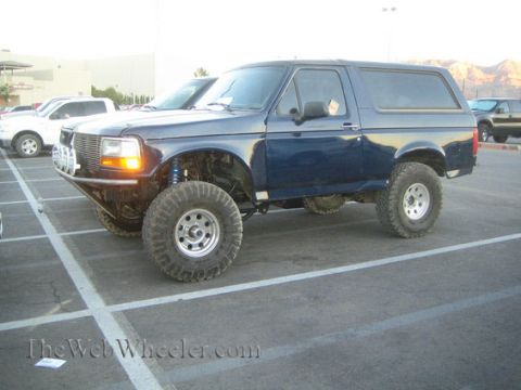 1990 Ford Bronco - dark blue lifted full-size Ford Bronco with a matching camper shell and large tires parked in a lot at dusk.