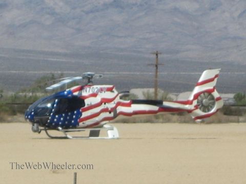 1990 Ford Bronco - helicopter painted with an American flag scheme and registration N702LV sits on the desert ground before distant mountains.