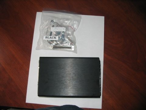 1991 Ford Bronco - A black electronic enclosure and a bag of connectors are placed on a white sheet of paper on a wooden surface.
