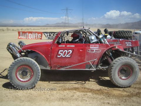 1990 Ford Bronco - red number 502 open-cockpit off-road race buggy with a visible engine sits in a desert pit area near a power line.