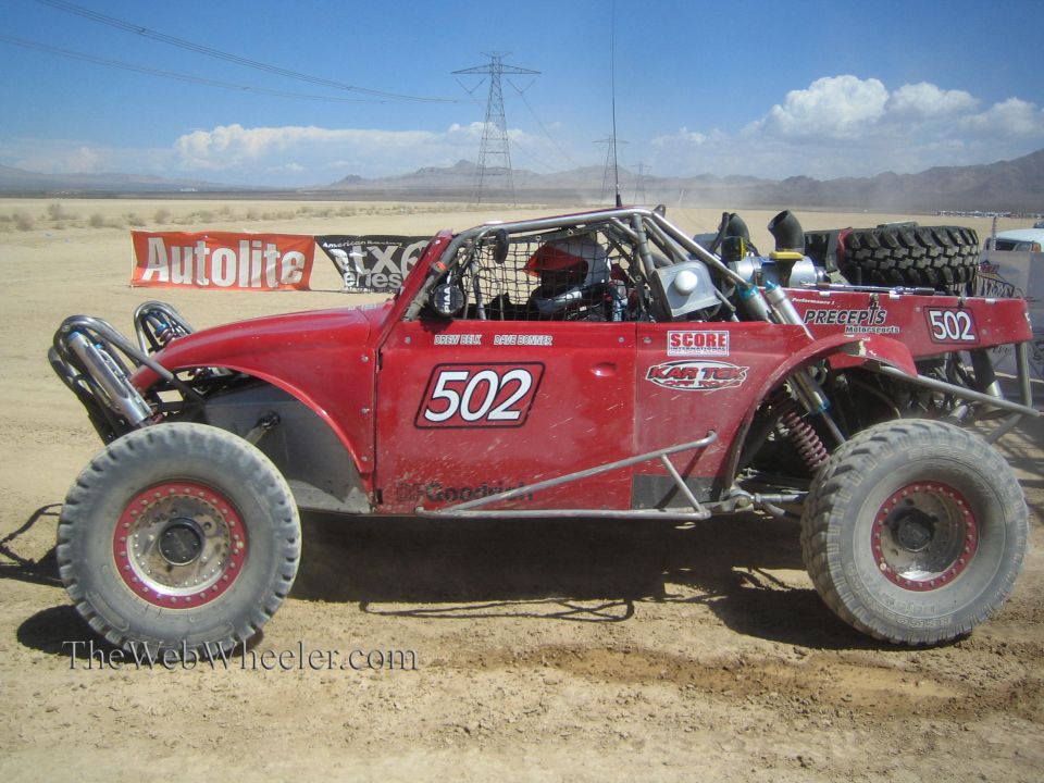 Red #502 open-cockpit off-road buggy parked in the desert pits