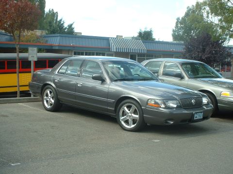 2000 Ford Crown Victoria - A gray 2000 Ford Crown Victoria is parked in a lot next to another vehicle.