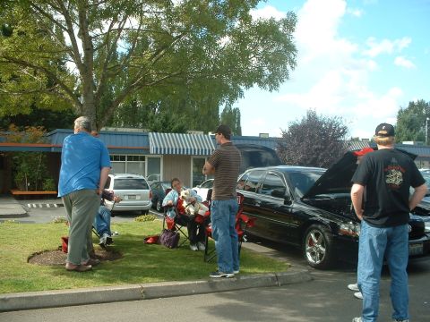 2000 Ford Crown Victoria - A group of people gather around a black sedan with its hood open at an outdoor event.
