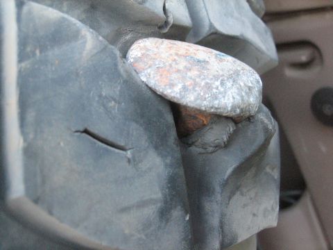 1995 Ford Bronco - A rusty nail is lodged in the tread of a vehicle tire, which also has a visible cut in the rubber.