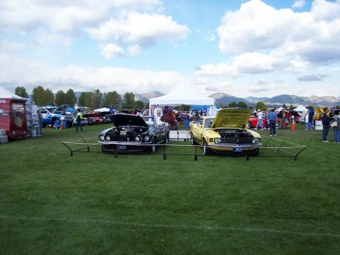1972 Ford Ranchero - Two classic cars, a yellow 1970 Ford Ranchero and a black car, are displayed outdoors at an event.