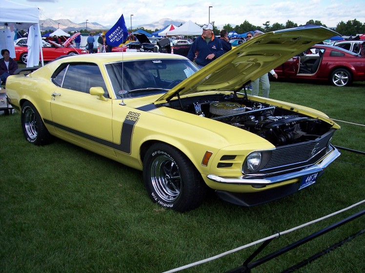Yellow 1970 Ford Mustang Boss 302, hood open, showing engine. "BOSS 302" text visible