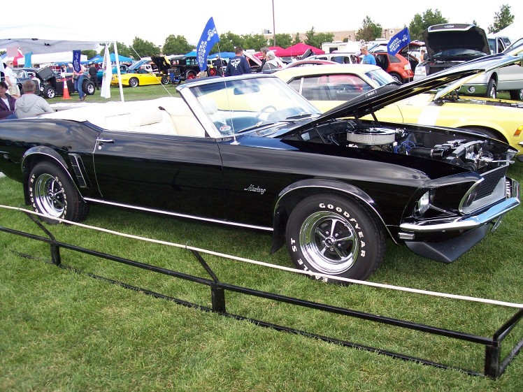 Black 1969 Ford Mustang convertible with white interior, hood open, parked on grass