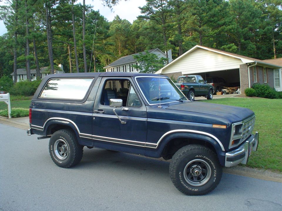 Dark blue Ford Bronco with hardtop and BFGoodrich A/T tires parked at a suburban curb