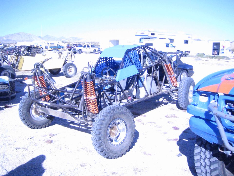 Open tube-frame off-road buggy with orange coilover shocks parked in desert pits