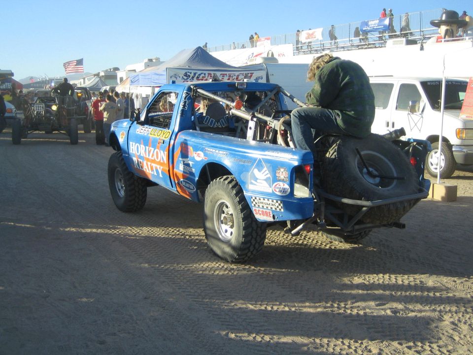 Blue Horizon Realty race truck with spare tire and rider at busy desert event