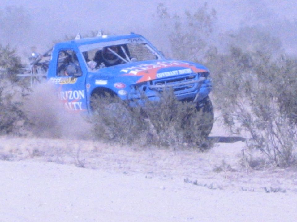 Blue Horizon Realty race truck racing through desert brush kicking up dust