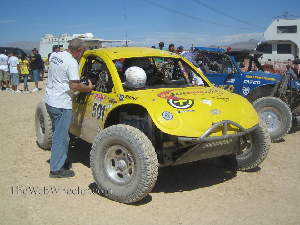 Yellow VW Beetle off-road race car #501 with helmeted driver and crewman in pits