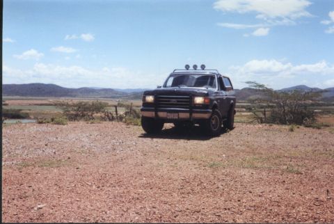 1990 Ford Bronco - A dark 1990 Ford Bronco is parked on a dirt lot with a scenic landscape in the background.
