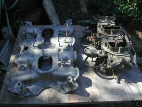 1972 Ford Ranchero - Two engine parts, an intake manifold and a carburetor assembly, are laid out on a wooden surface outdoors.