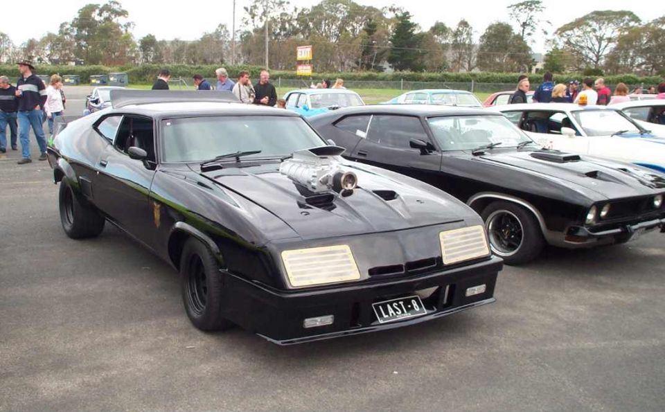 Modified black coupe with prominent supercharger on hood, parked next to other cars