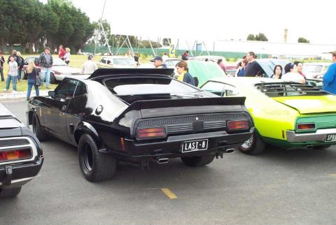 1972 Ford Ranchero - A black coupe with a prominent spoiler and dual exhaust pipes is parked at an outdoor car show.