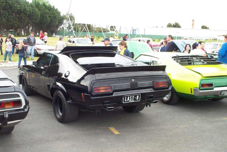 black coupe with spoiler and custom plate 'LAST-8' parked next to a green convertible
