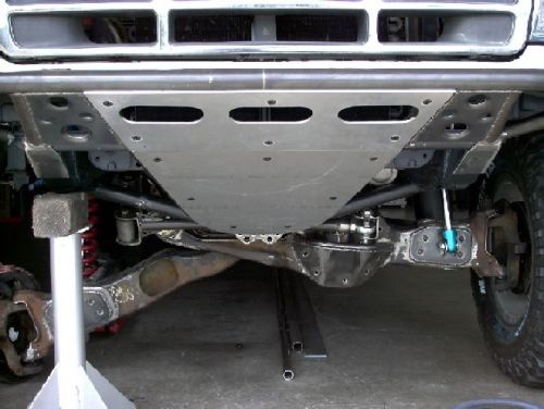 Underside of a vehicle with aftermarket skid plates and suspension components. The front grille is visible