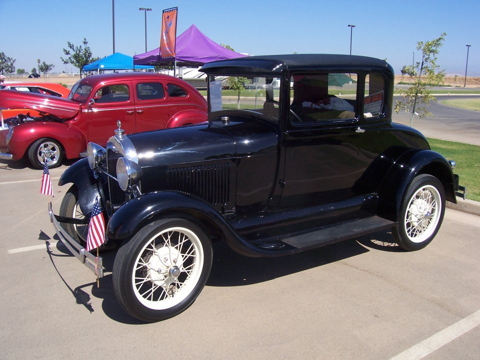Black 1928 coupe with white wire wheels and American flags on the bumper