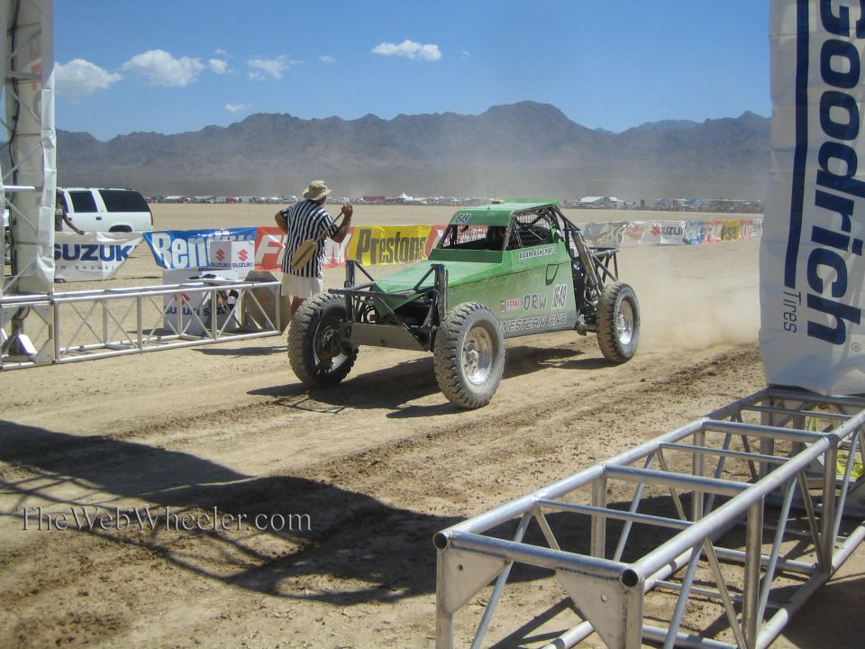 Green tube-frame off-road buggy on dusty desert course past BFGoodrich banner