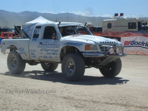 1990 Ford Bronco - white off-road race truck numbered 758, lettered Sierra Brothers Racing, drives across a dusty desert course.