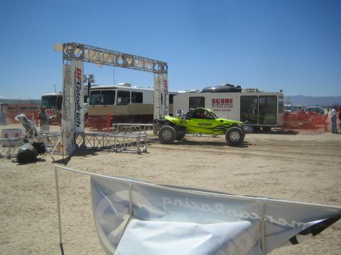 1990 Ford Bronco - green off-road buggy numbered 1015 sits under a BFGoodrich start gate near the SCORE media center trailer.