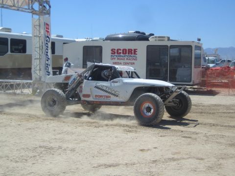 1990 Ford Bronco - white tube-frame off-road buggy throws up dust as it passes the SCORE International media center in the desert.